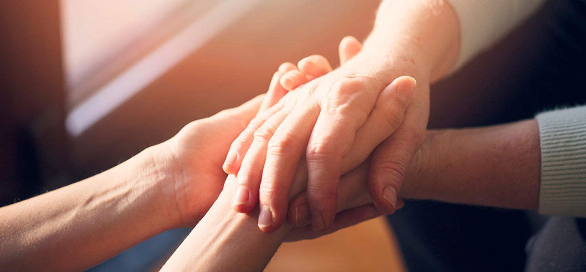 Two sets of hands facing one another and interlocking with filtered lightness hitting the skin through the window.