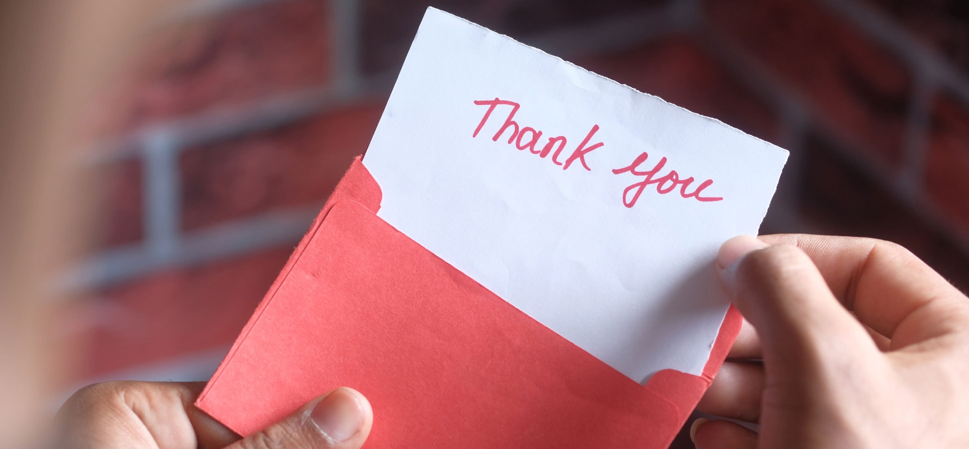 Person holding envelope and pulling out a card with the words thank you written on it