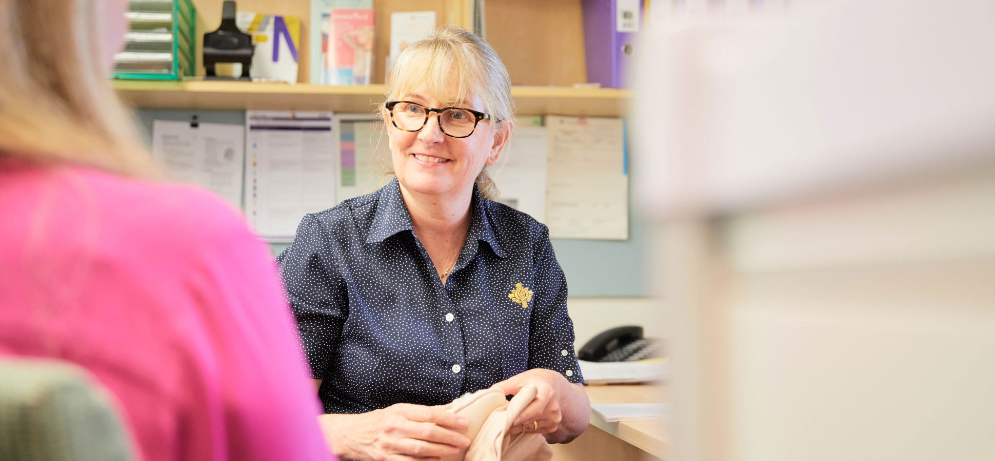 Nursing caregiver at desk with book talking to patient