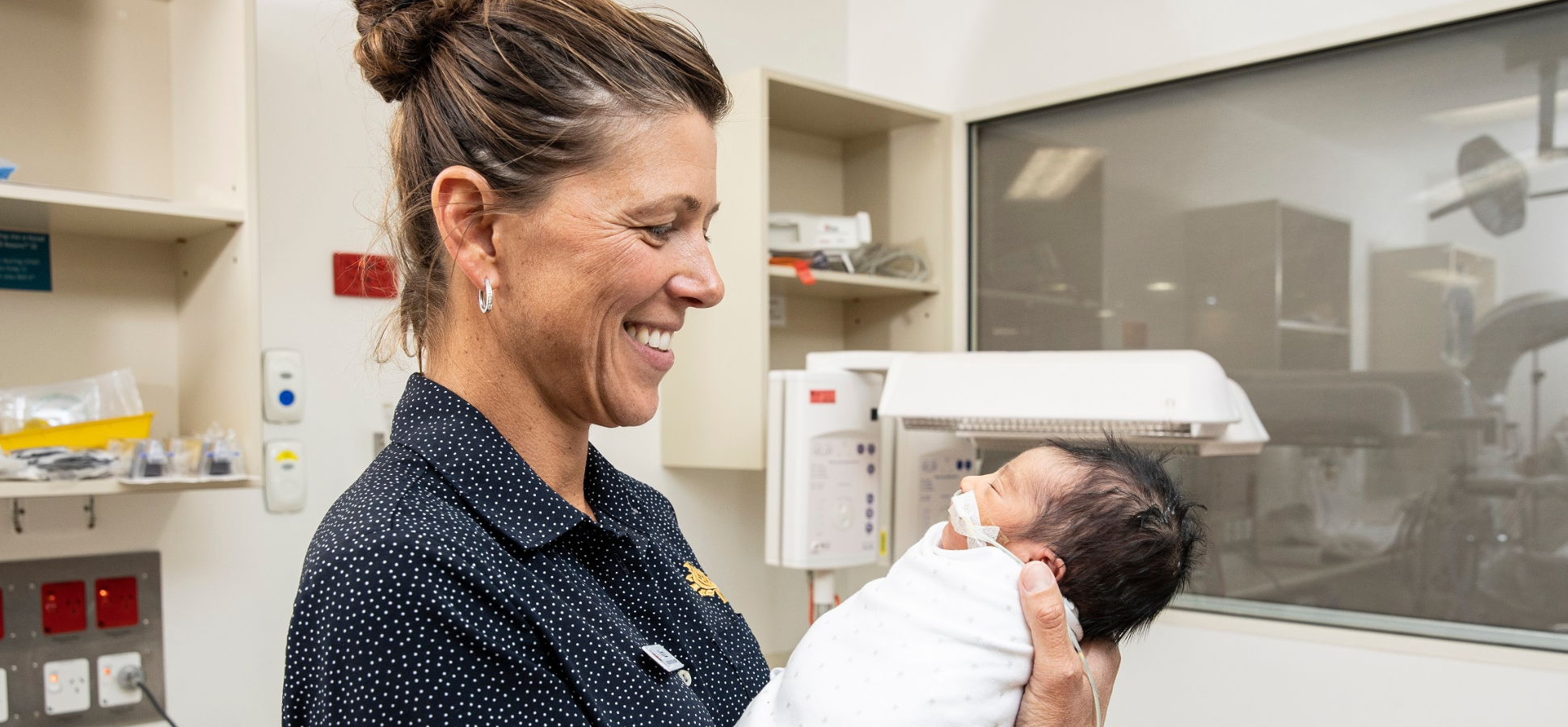 Caregiver cradling a swaddled newborn and smiling