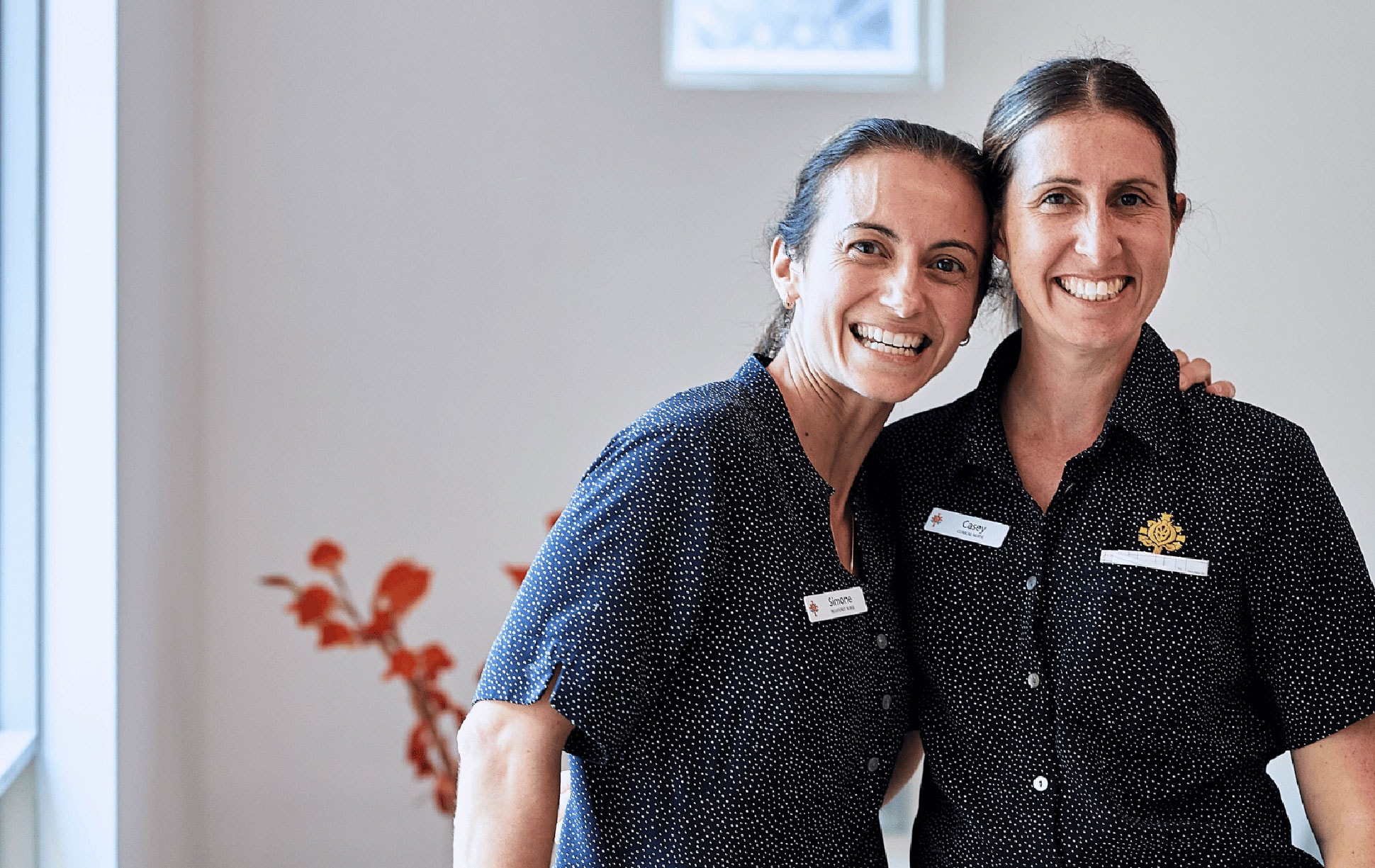 Two caregivers with arms around one another looking cheery