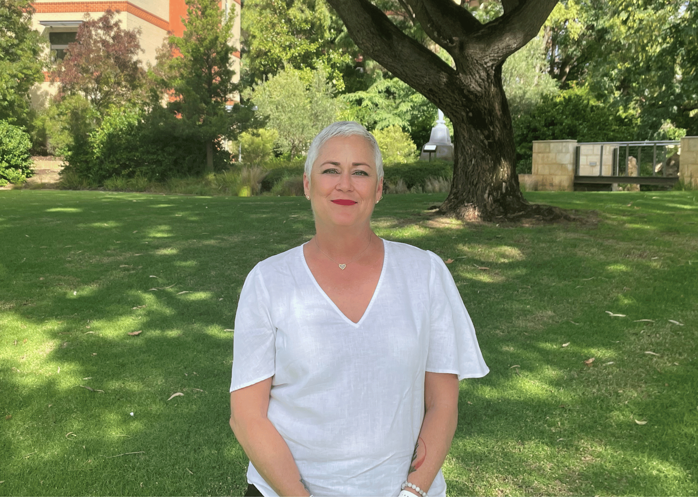 Woman standing outside on grass under shady tree smiling at camera