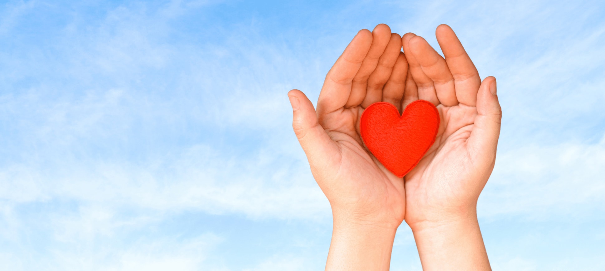 Hands cradling a red felt heart against a backdrop of a blue sky