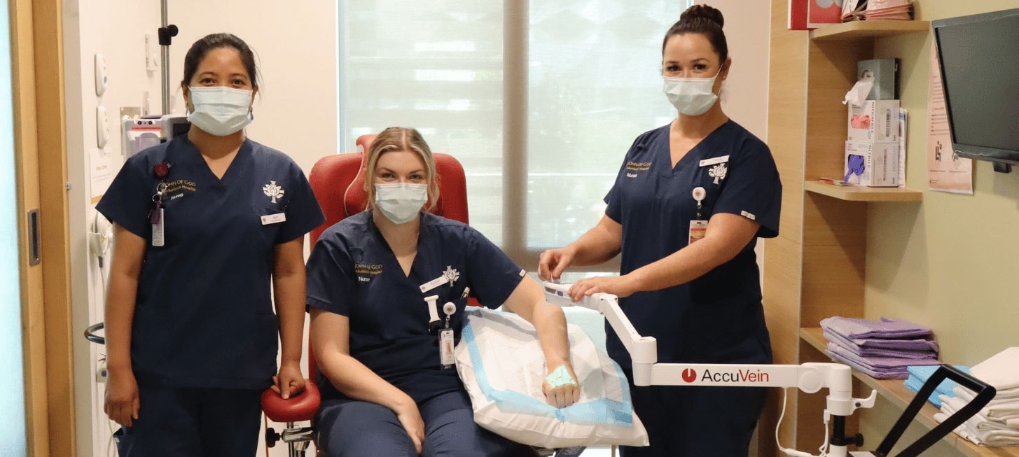 Two nurses standing, one sitting in a chair with her hand under the AccuVein Finder machine