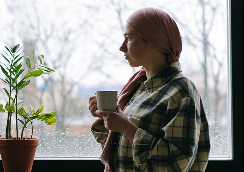 A cancer patient holds a cup of tea while gazing out the window