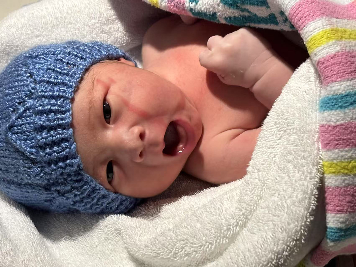 A crying newborn baby with a blue wool hat