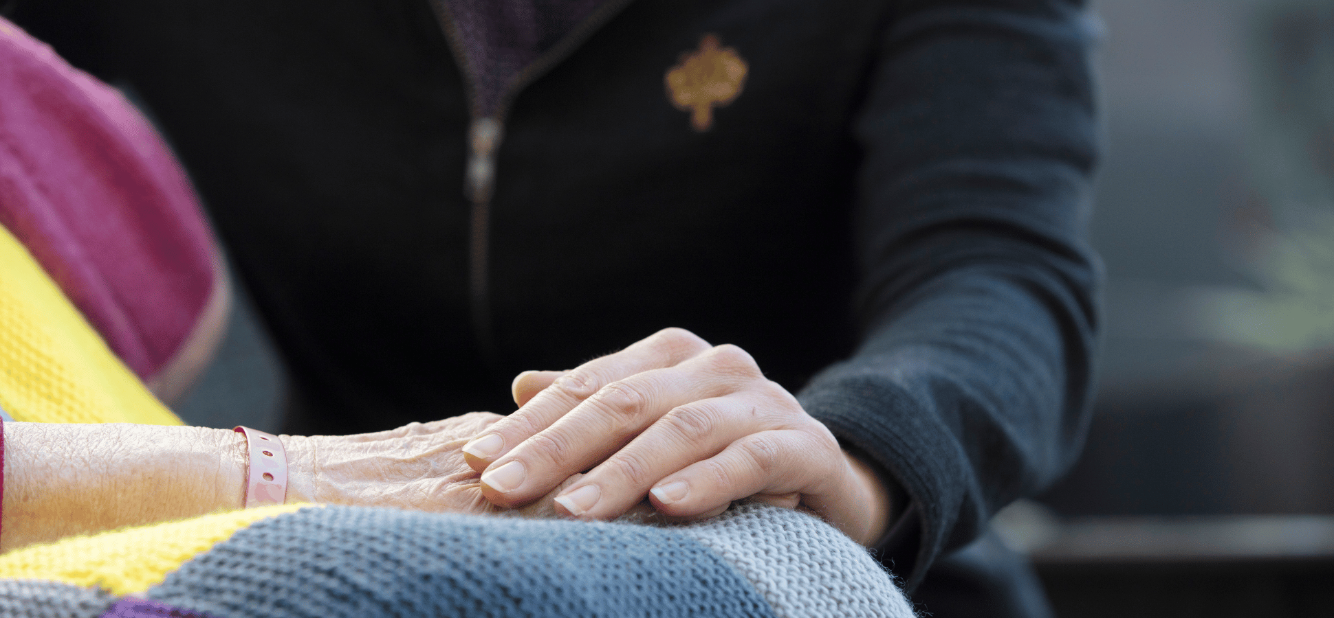 Caregiver resting a hand on another person's hand in their lap