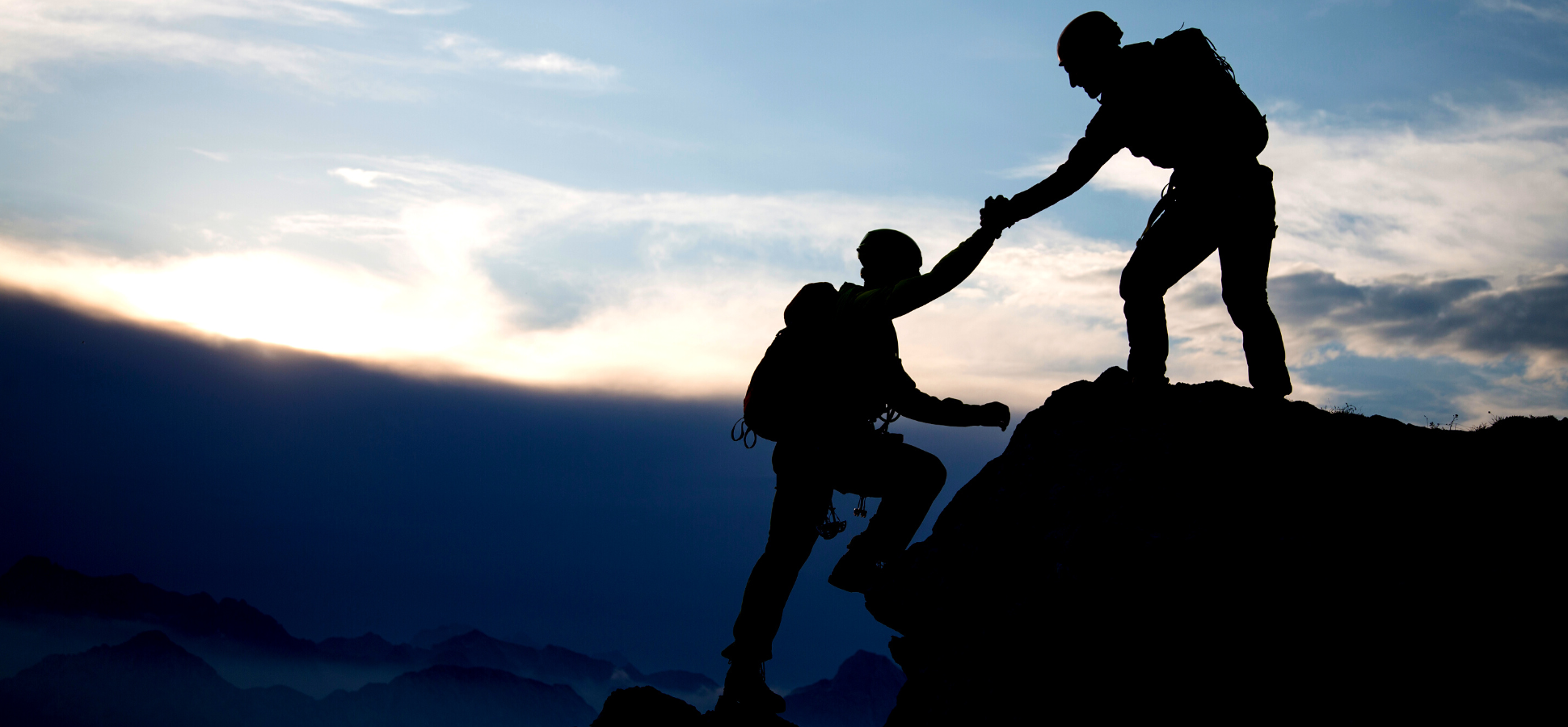 Two mountain climbers helping each other up a mountain