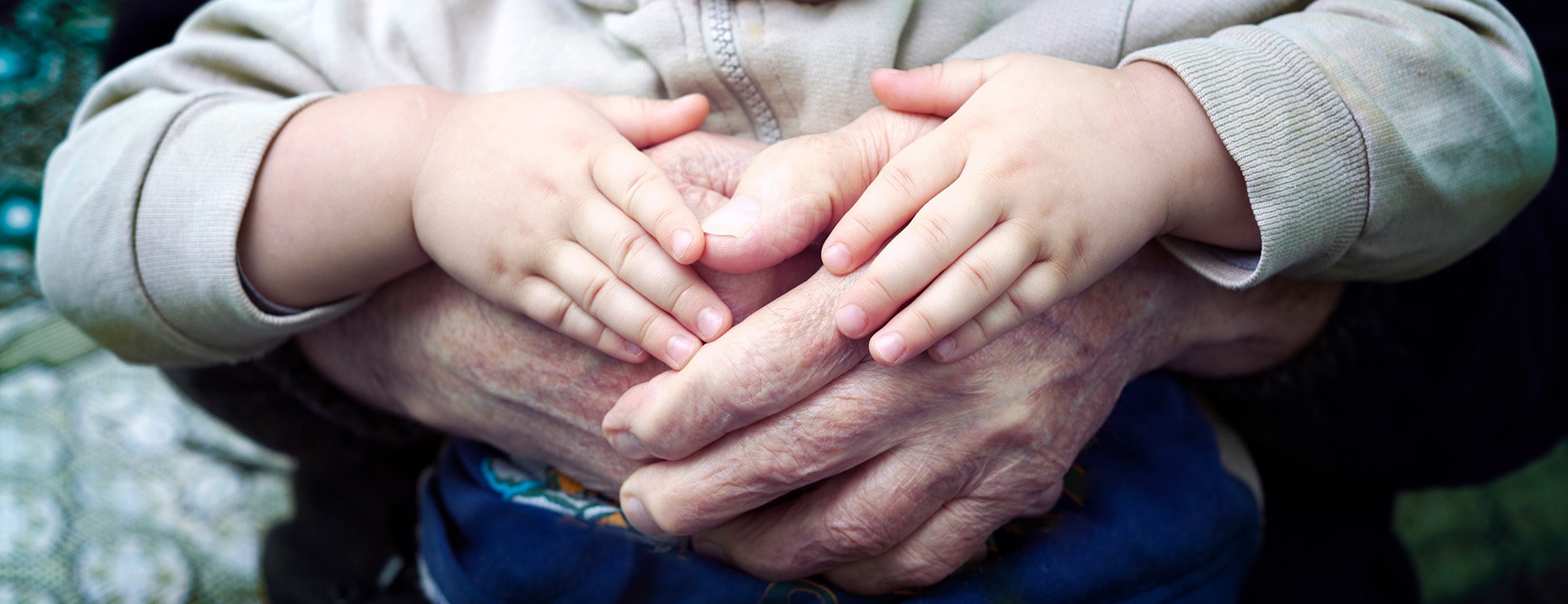 A close up shot of a person with their hands wrapped around a small child, with the child's hands on the person's hands.