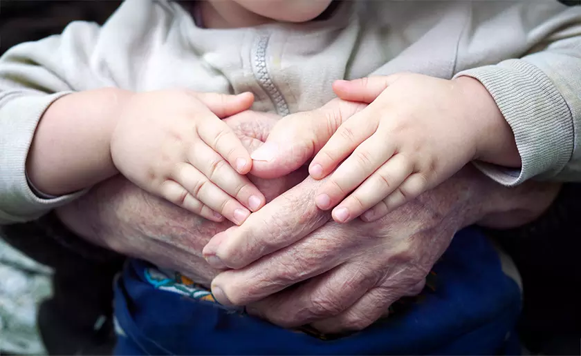 A pair of small children's hands rests over a pair of old hands.
