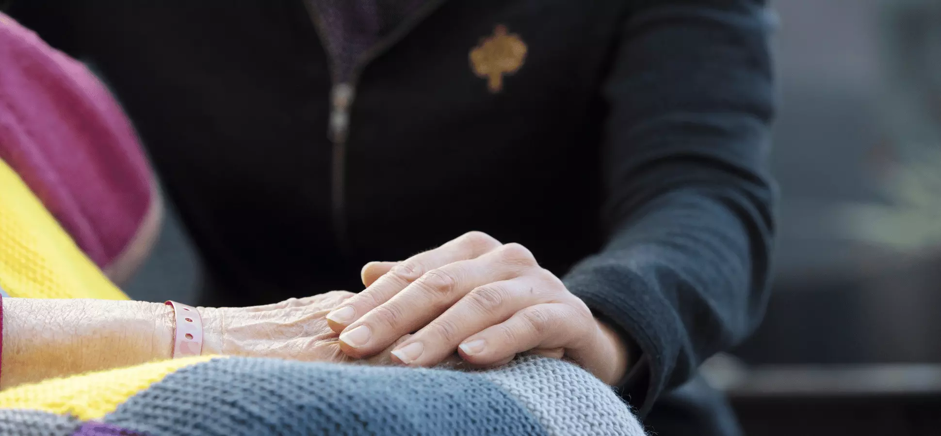 Caregiver resting a hand on another person’s hand in their lap.