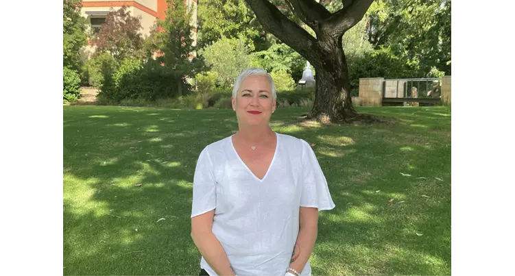 Woman standing outside on grass under shady tree smiling at camera.