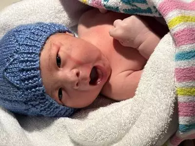 A crying newborn baby with a blue wool hat.