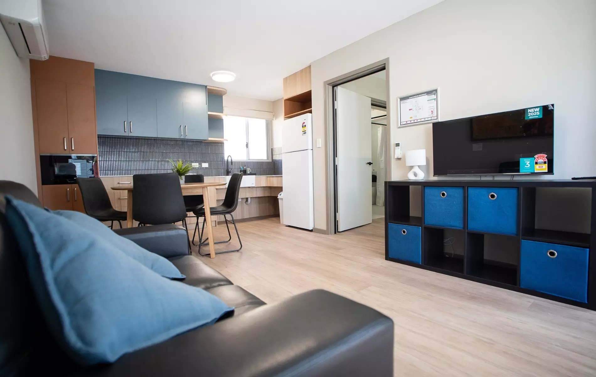 A modern looking room with a kitchen, couch, tv and dining table.