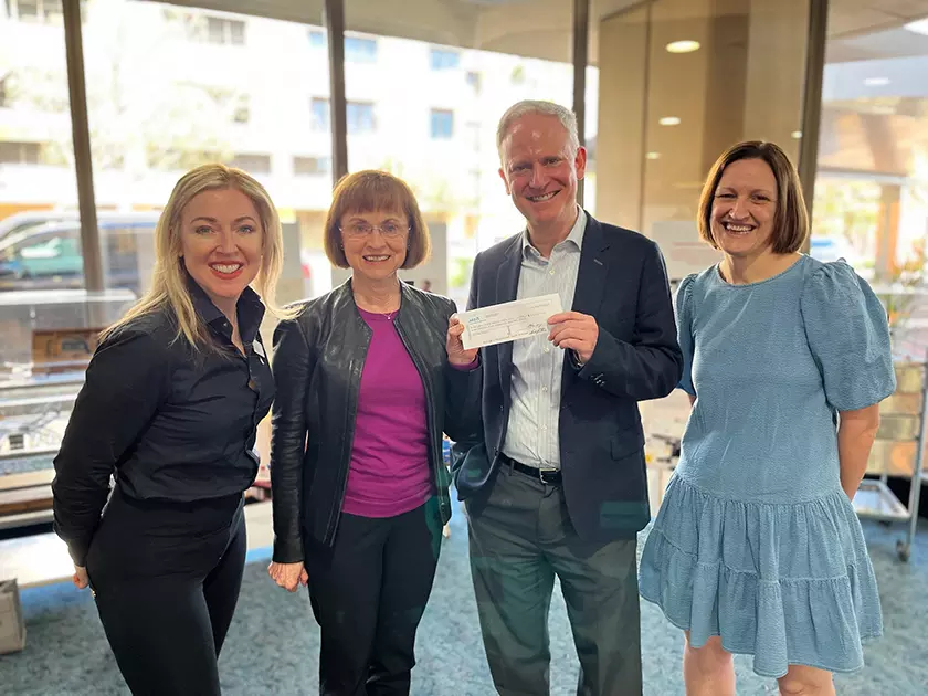 Four people standing in a room smiling at the camera, with one of them holding a cheque up.
