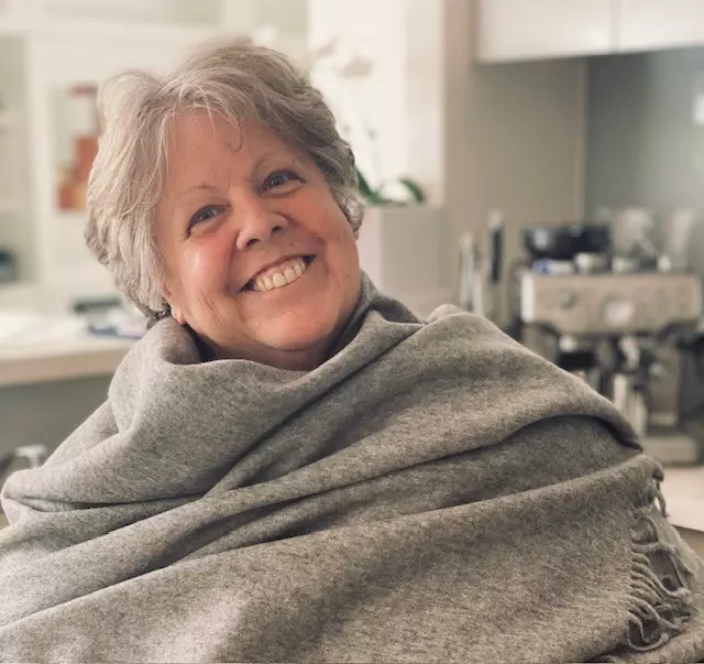 Image of Pauline Tew smiling with a grey blanket wrapped around her.