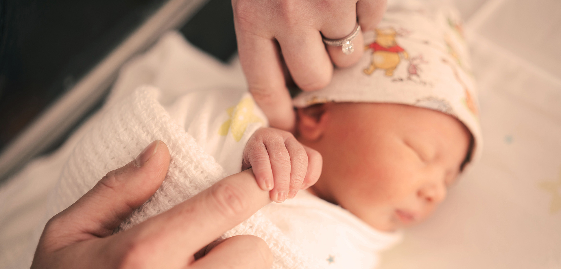 A newborn baby holding an adult's finger
