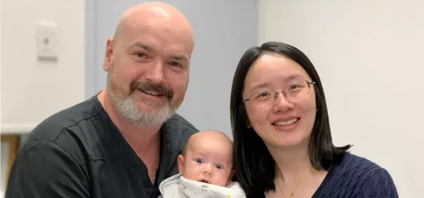 Two people smiling at the camera with a baby