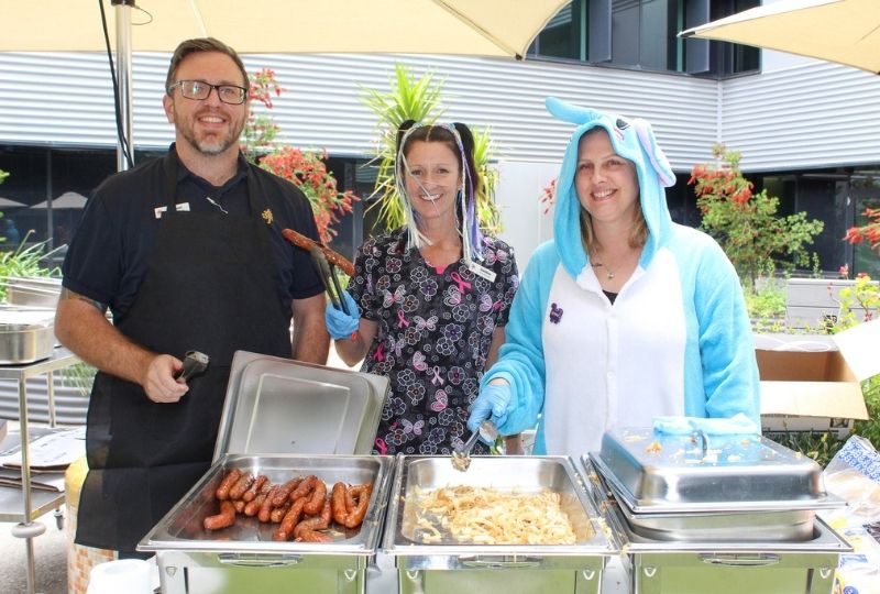 Three caregivers outside with sausages and onions